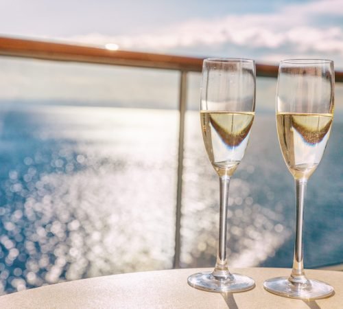 Luxury cruise ship travel champagne glasses on balcony deck with ocean sunset view on Caribbean vacation. Drinks in sun flare on cruise holiday destination.