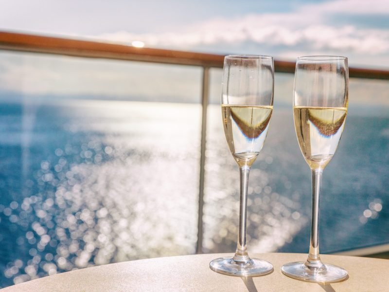 Luxury cruise ship travel champagne glasses on balcony deck with ocean sunset view on Caribbean vacation. Drinks in sun flare on cruise holiday destination.